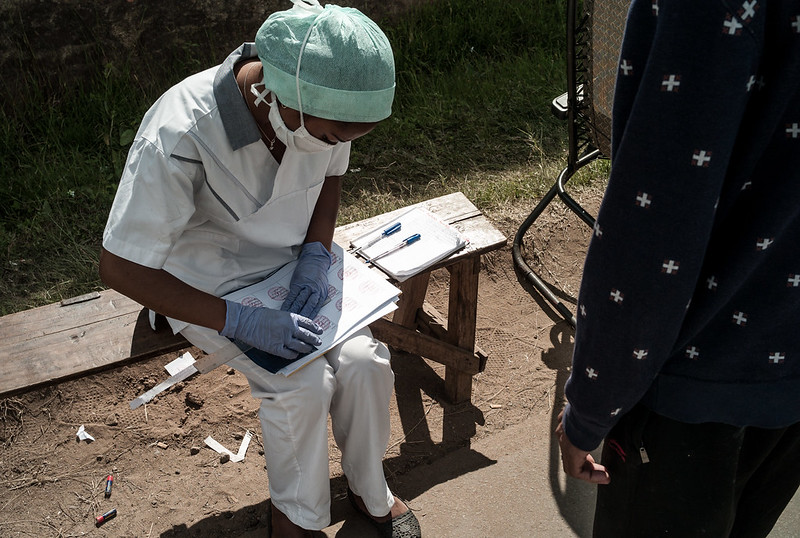 A healthcare worker wearing a facemask and reviewing a document while sitting on a bench in the community. Photo Credit: World Bank